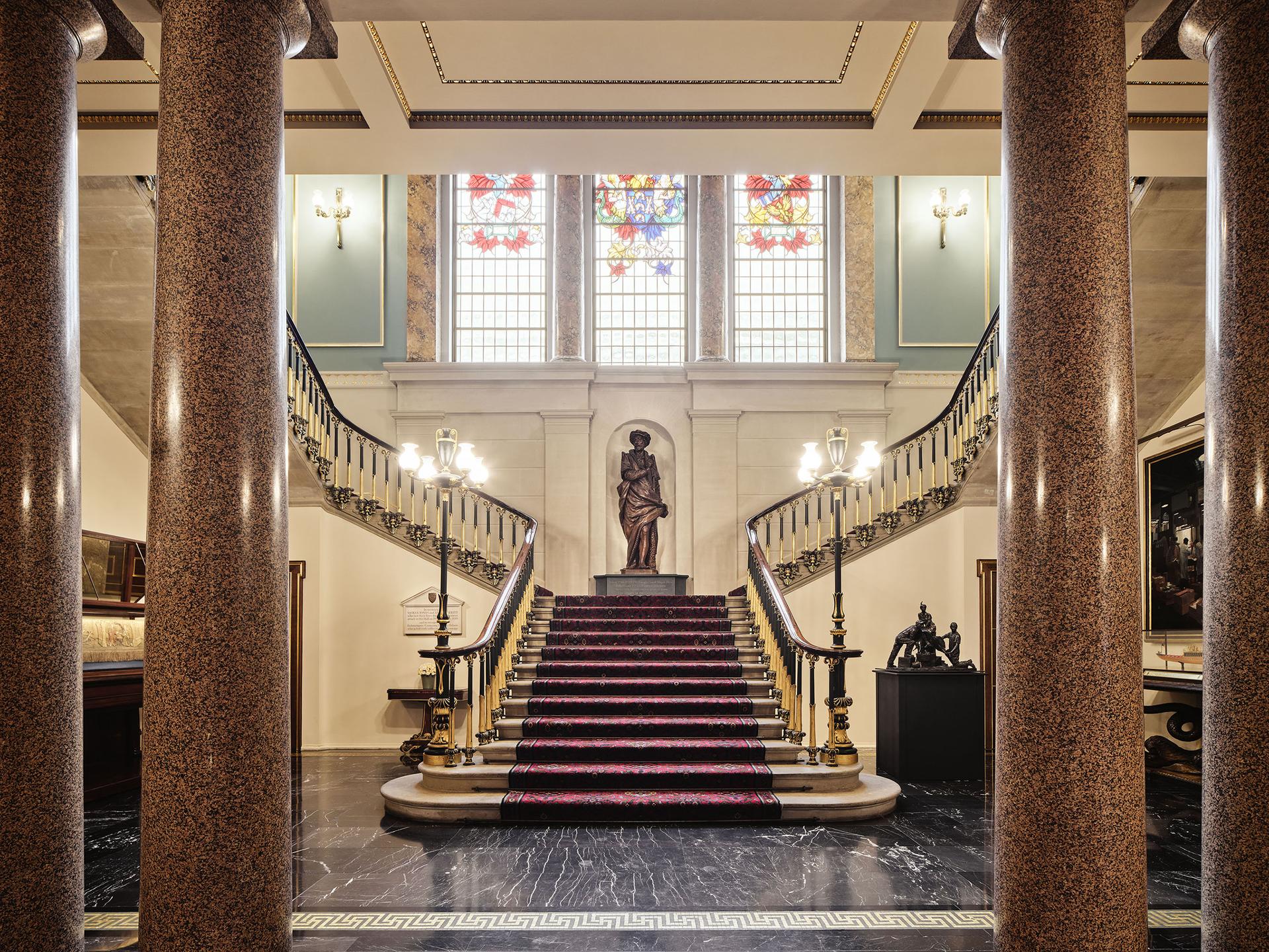 Newly refined staircase hall showing a grand staircase, brass statues and marble columns