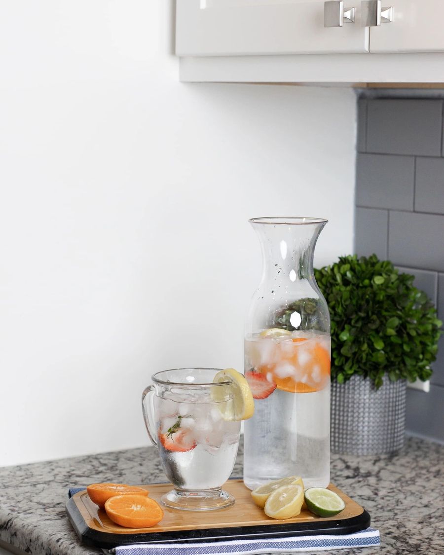 A glass carafe and cup of iced water with citrus on a kitchen counter