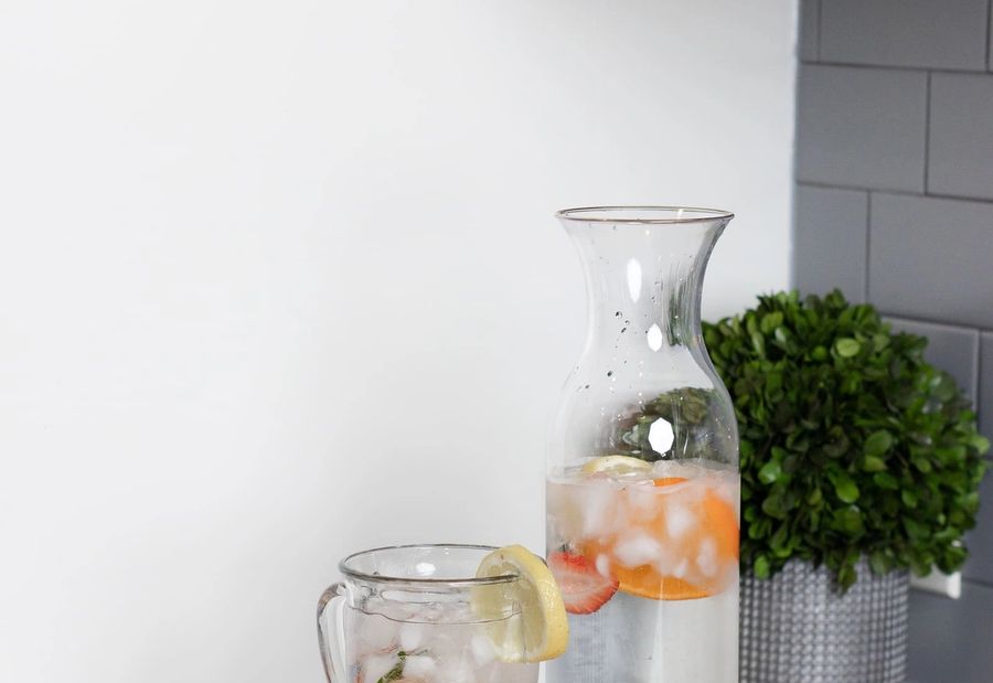 A glass carafe and cup of iced water with citrus on a kitchen counter