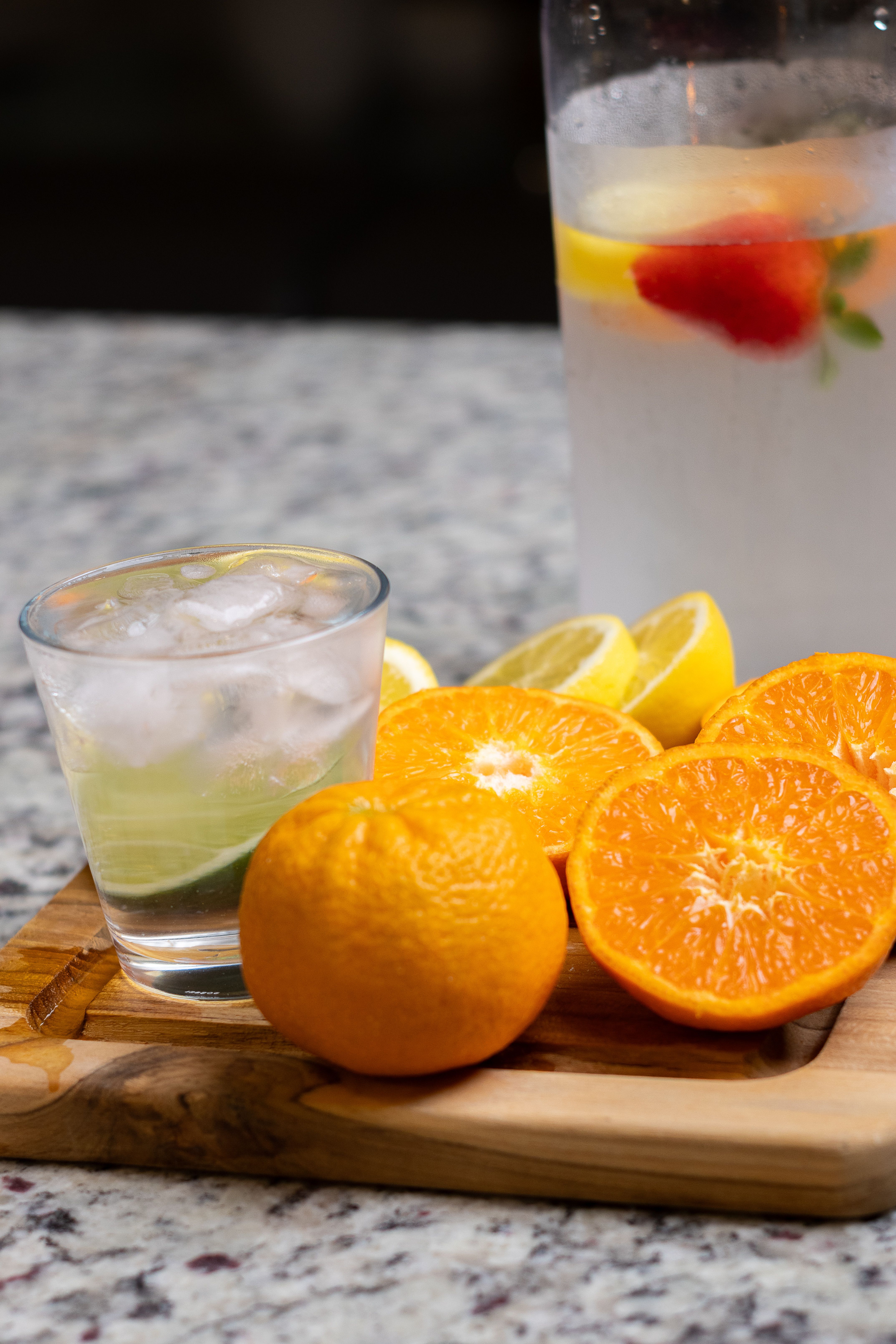 A clear glass with ice and sliced citrus on a wooden board. A cold drink, composed.