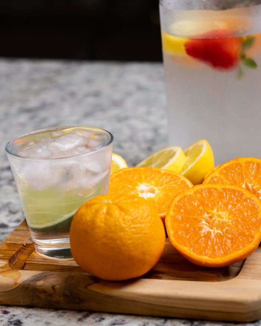 A clear glass with ice and sliced citrus on a wooden board. A cold drink, composed.