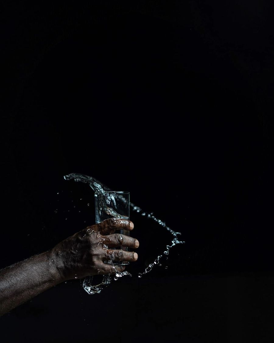 A hand holding a clear glass of water against a dark background, with water splashing around the glass.