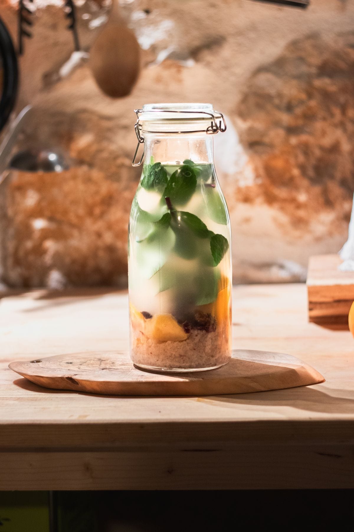 A swing top bottle of homemade water kefir, kefir grains settled at the bottom with fruit pieces and fresh mint inside.