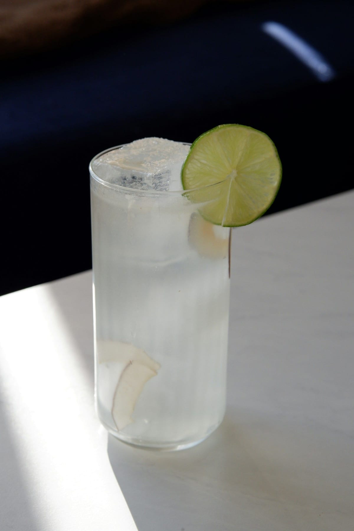 A tall glass of fresh coconut water over ice, coconut slivers floating inside and a lime wheel on the rim.