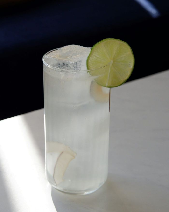 A tall glass of fresh coconut water over ice, coconut slivers floating inside and a lime wheel on the rim.