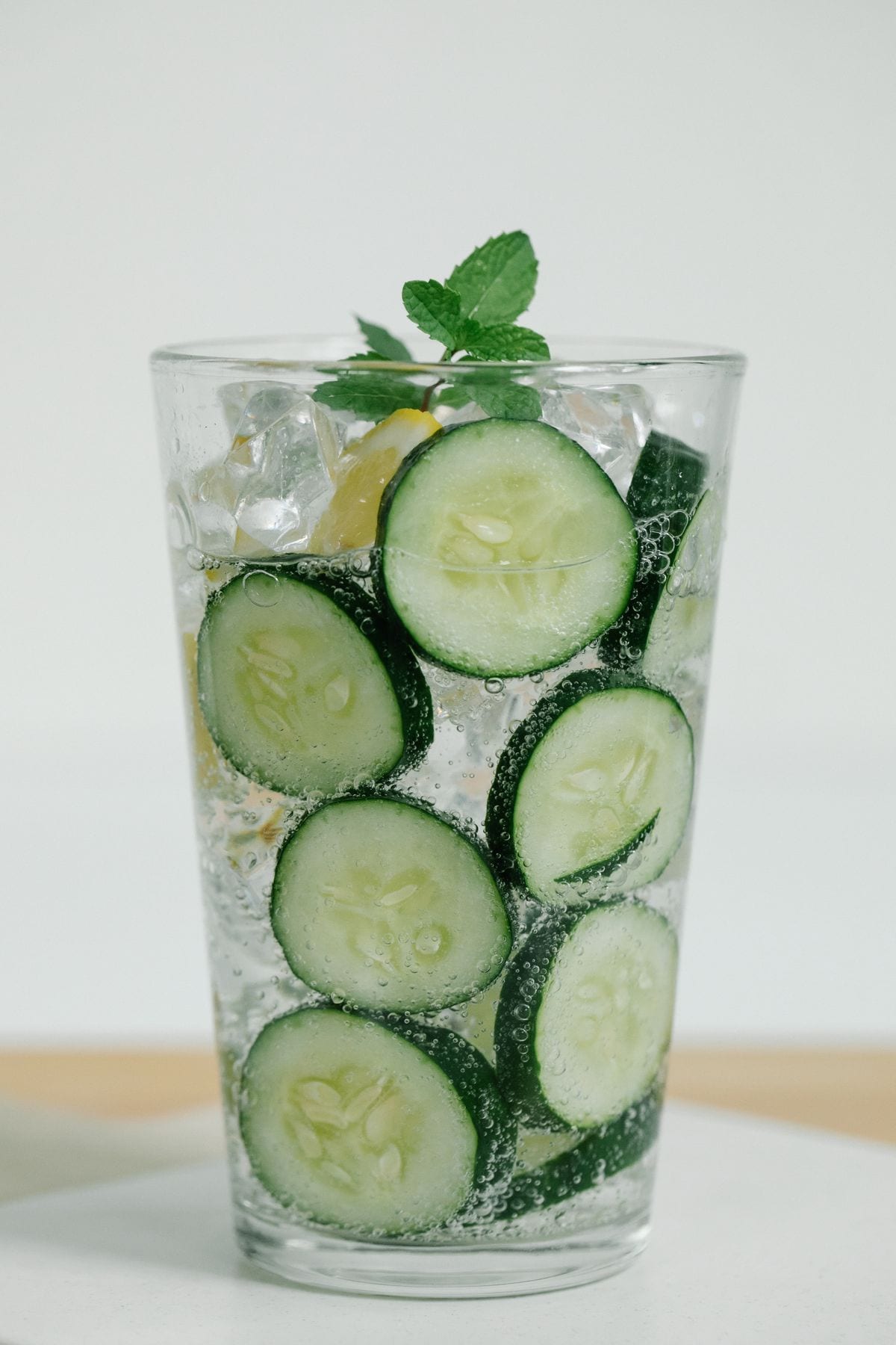 A tall glass of sparkling water packed with cucumber slices and ice, topped with a sprig of fresh mint.
