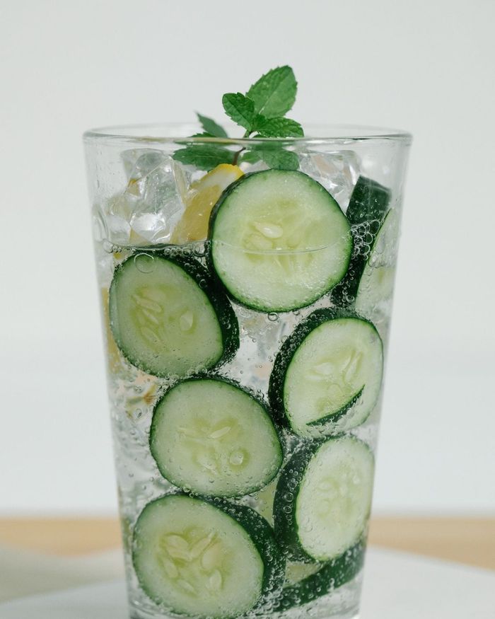 A tall glass of sparkling water packed with cucumber slices and ice, topped with a sprig of fresh mint.