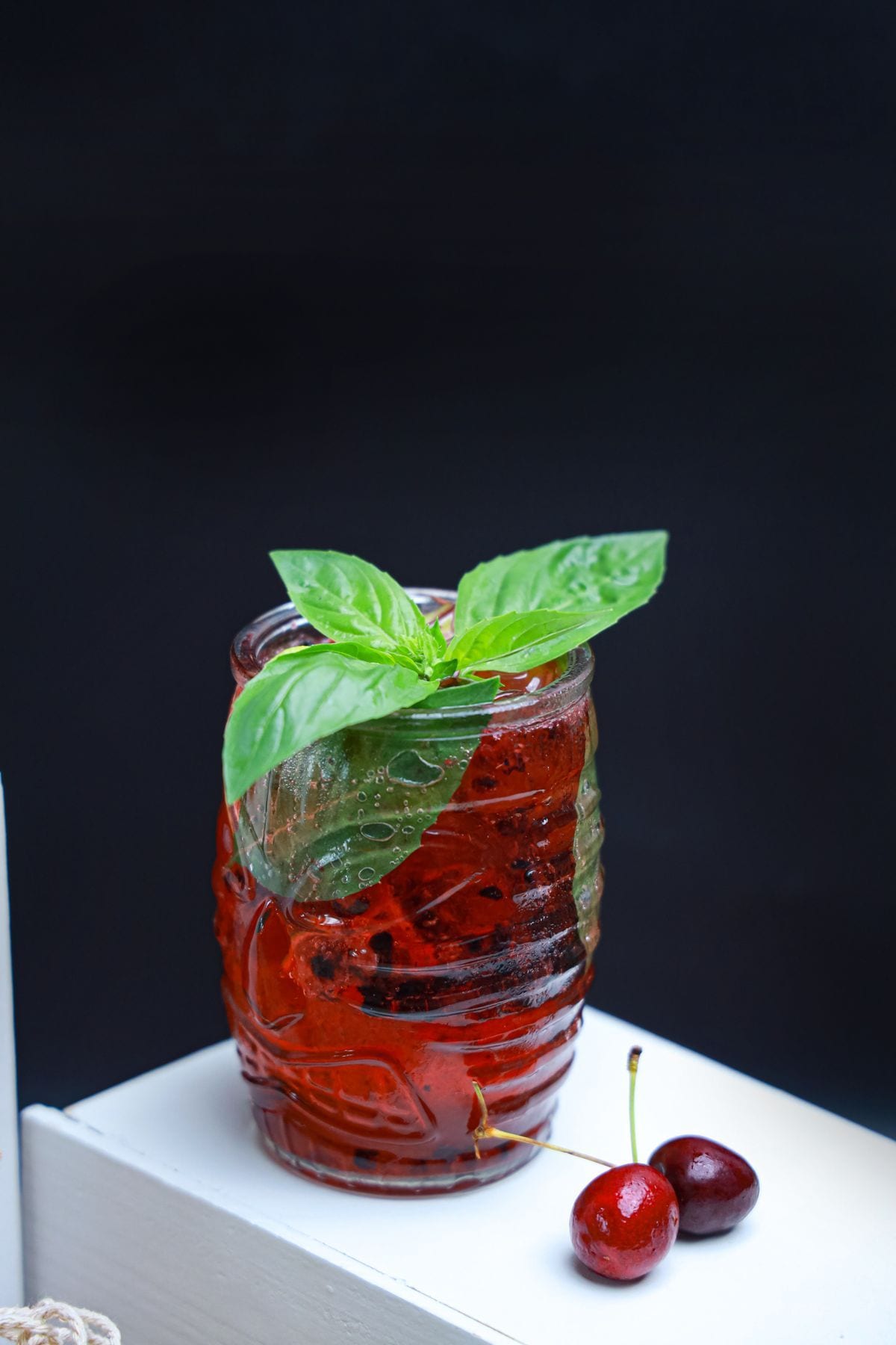 A jar glass of chilled ruby red berry water, dark berries muddled inside, crowned with fresh basil leaves.