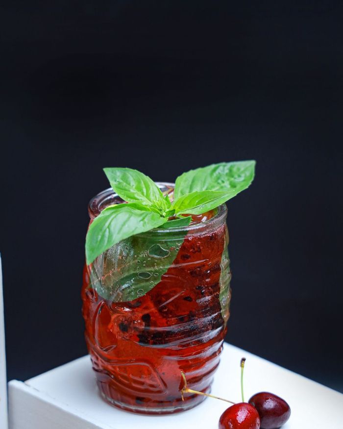 A jar glass of chilled ruby red berry water, dark berries muddled inside, crowned with fresh basil leaves.