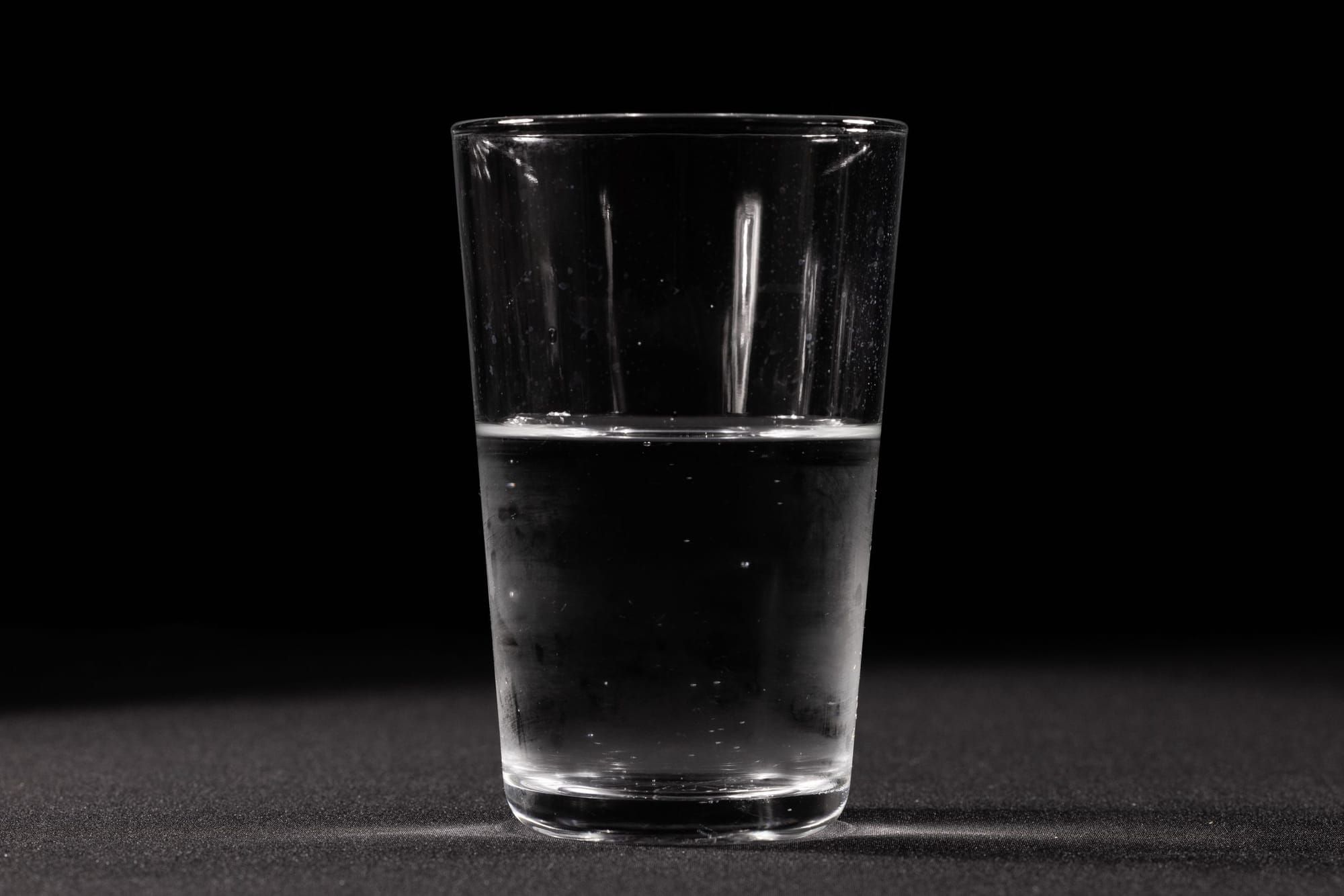 A clear glass of plain drinking water on a dark surface, lit from one side.