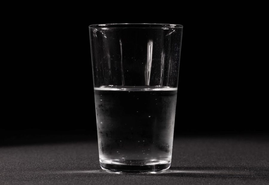 A clear glass of plain drinking water on a dark surface, lit from one side.