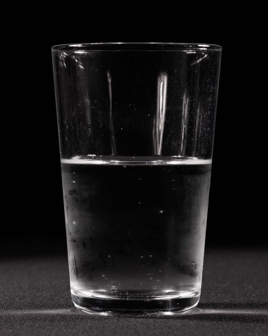 A clear glass of plain drinking water on a dark surface, lit from one side.