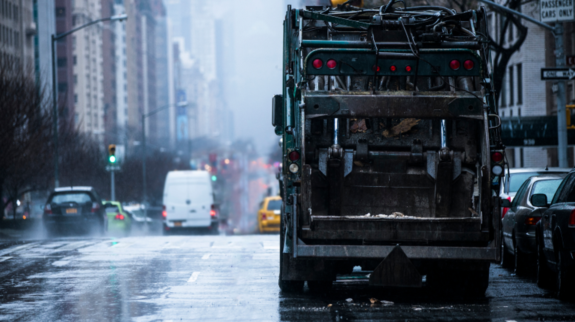 Cyclist riding behind garbage truck in the rain