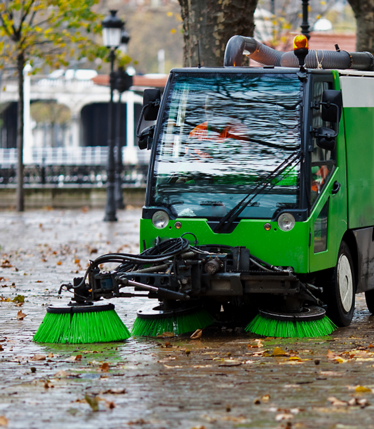 Small green street sweeper on rainy sidewalk