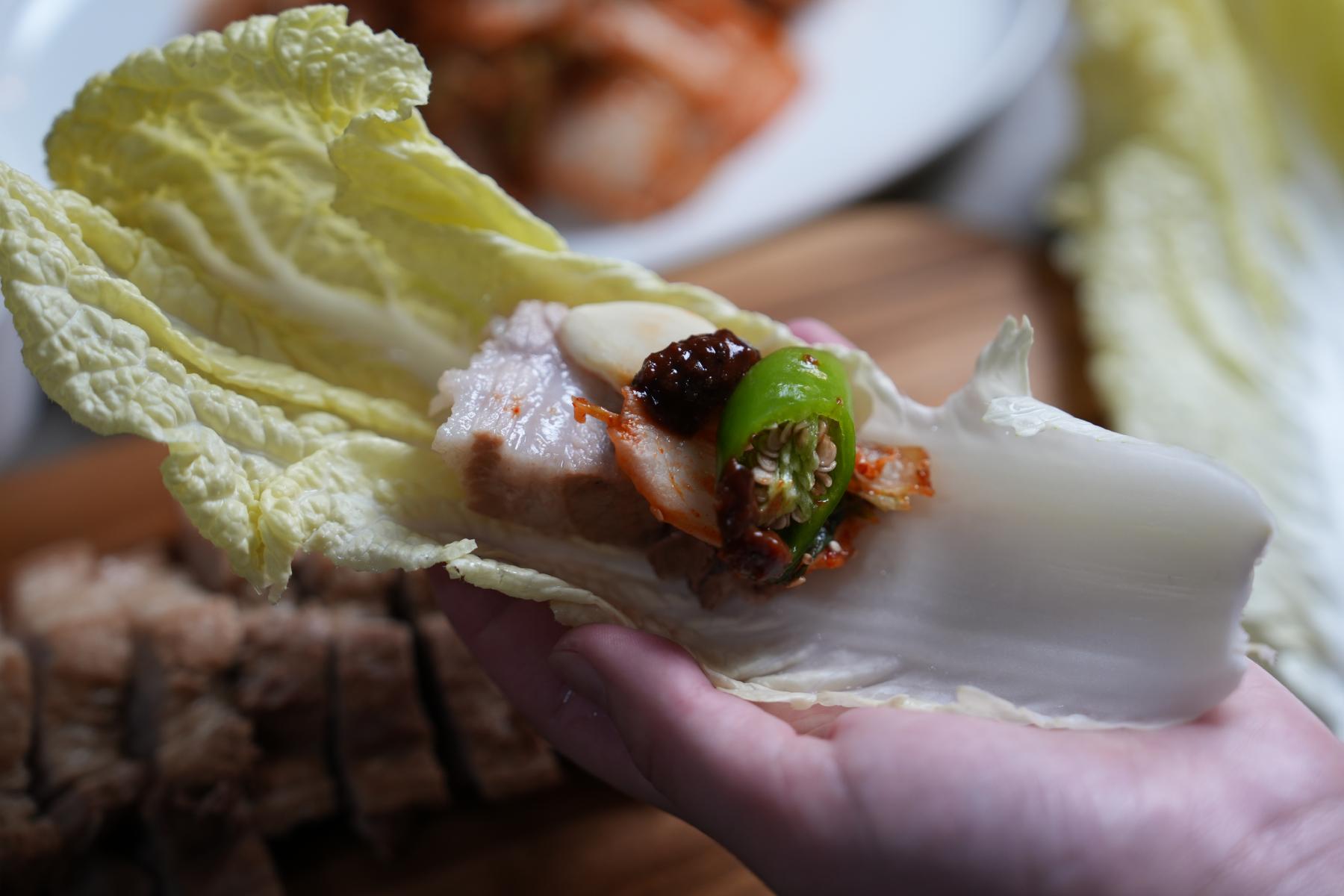 Wrap kimchi, pepper, garlic, ssamjang and meat with napa cabbage