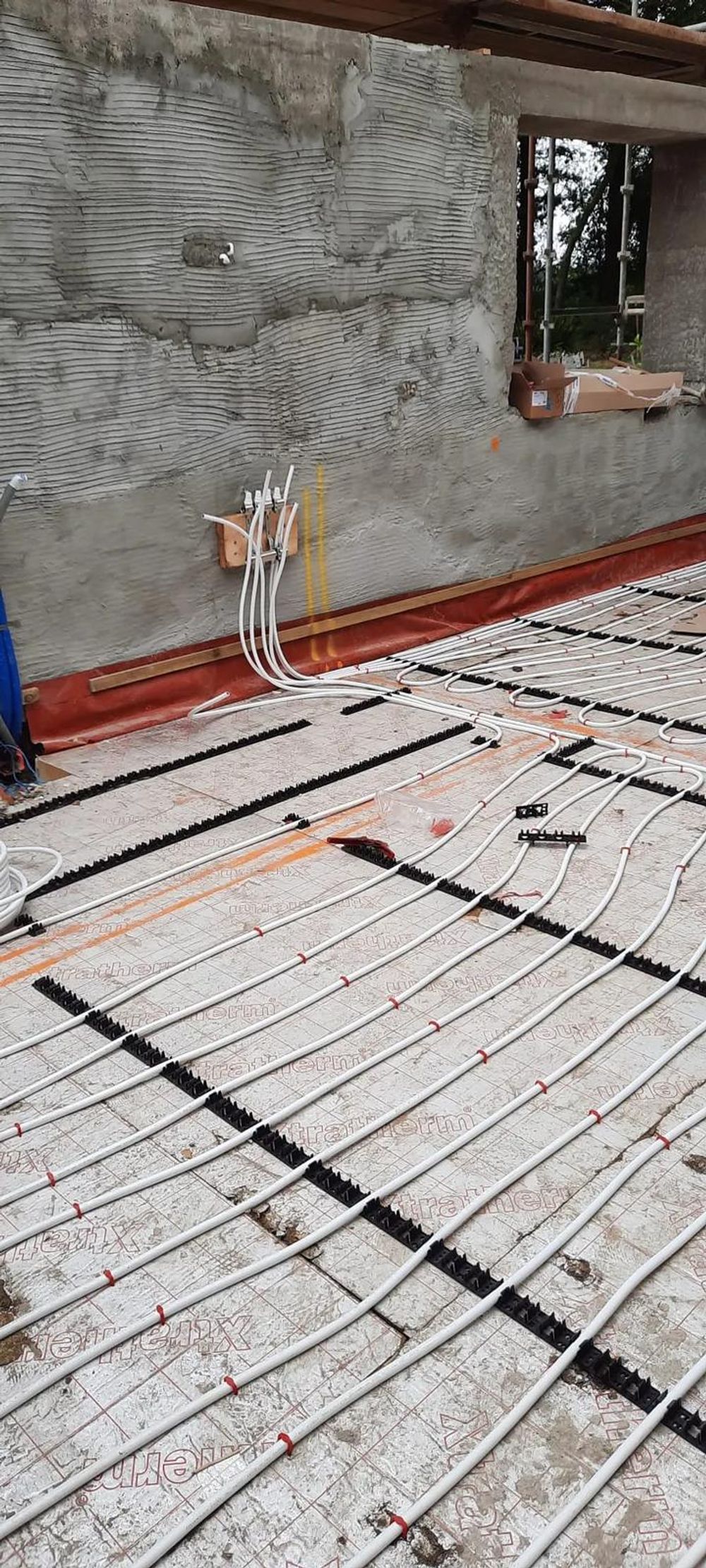 Underfloor heating pipes running to the manifold at a rendered wall