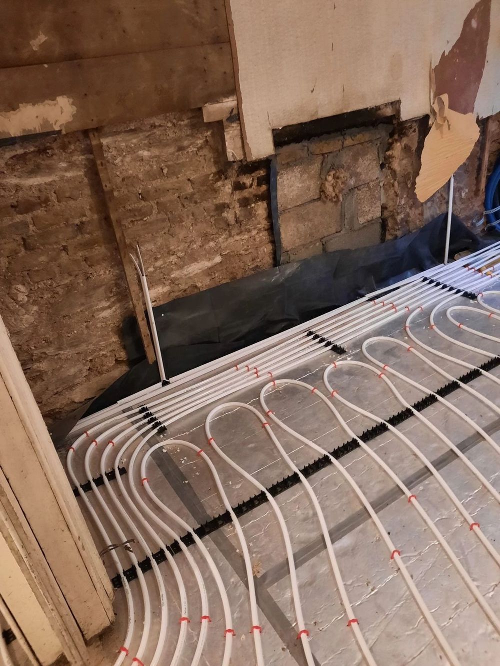Underfloor heating pipes laid beside an old stone wall
