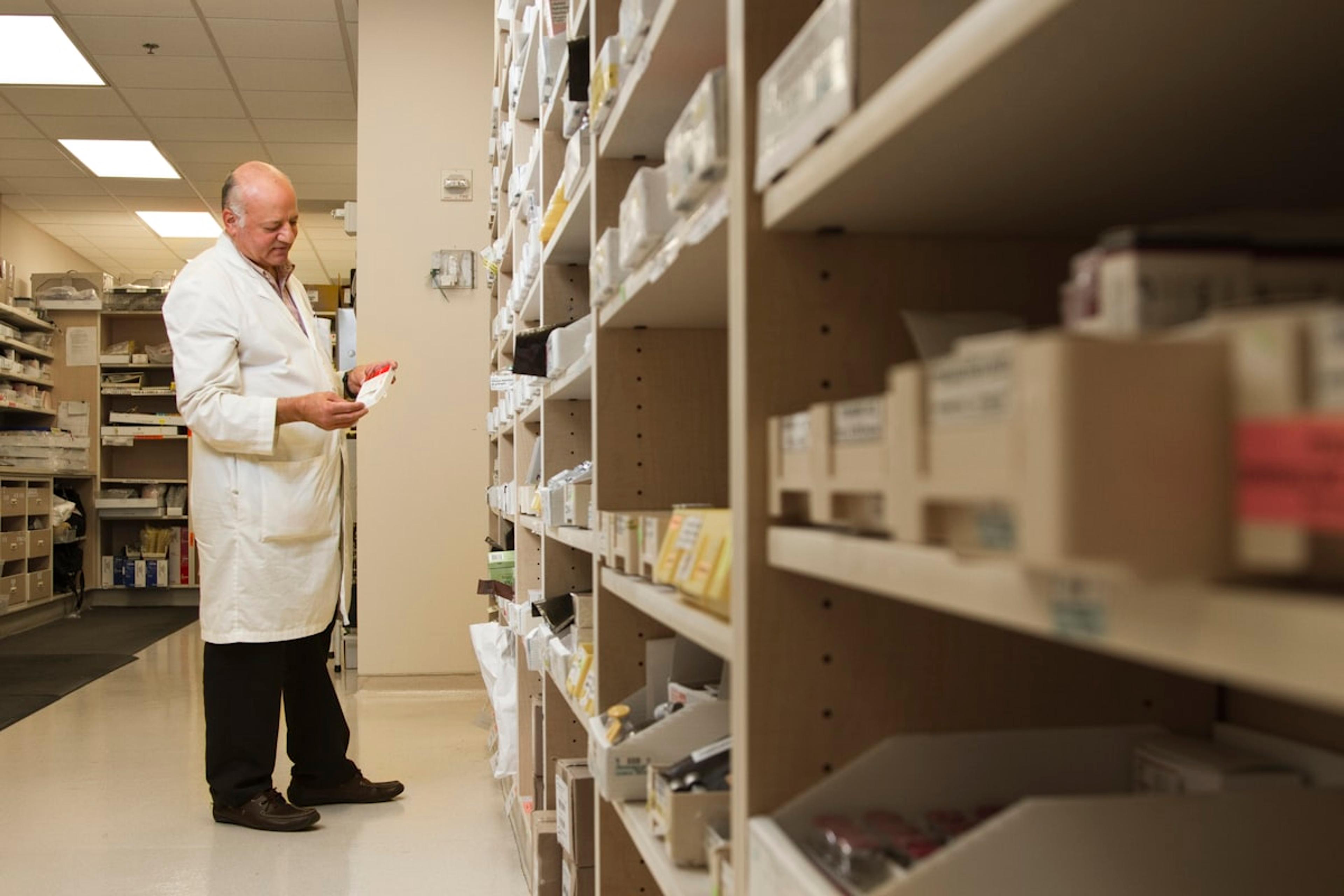 A pharmacist beside a shelf of medicines