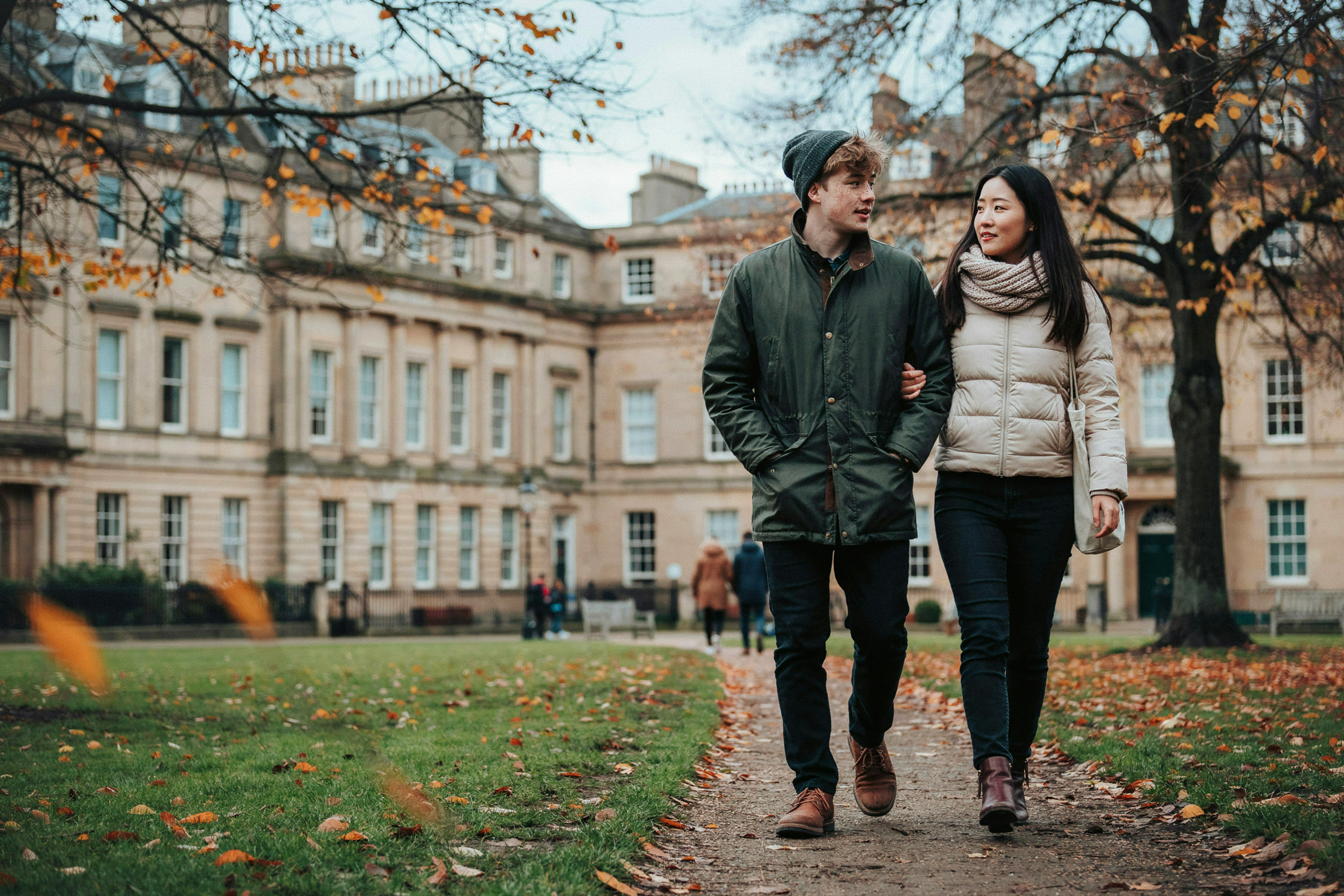 Two students walking through George Square Gardens in Edinburgh in autumn