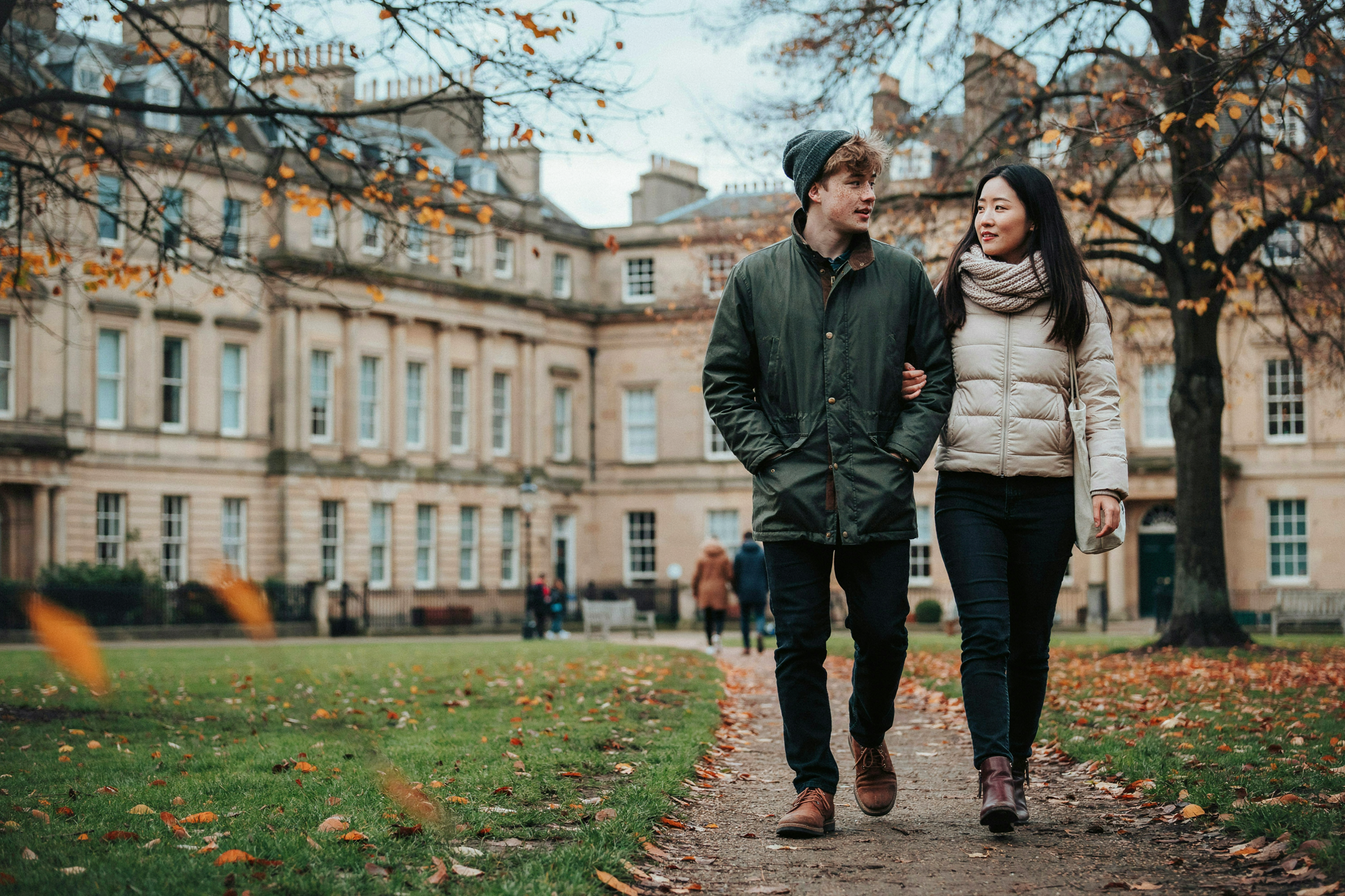 Two students walking through George Square Gardens in Edinburgh in autumn