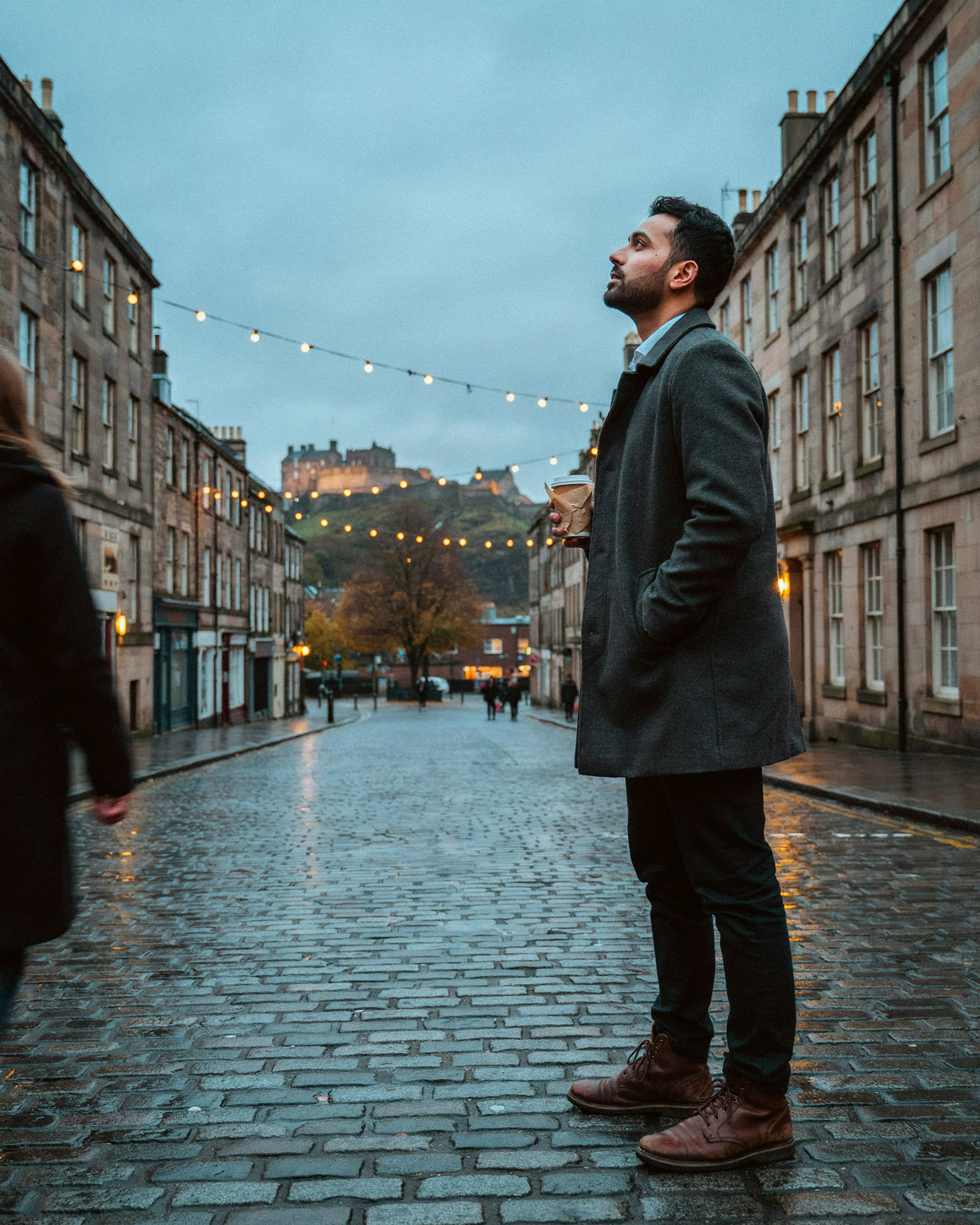 Hospitality worker in the Grassmarket at dusk in winter with Edinburgh Castle lit behind