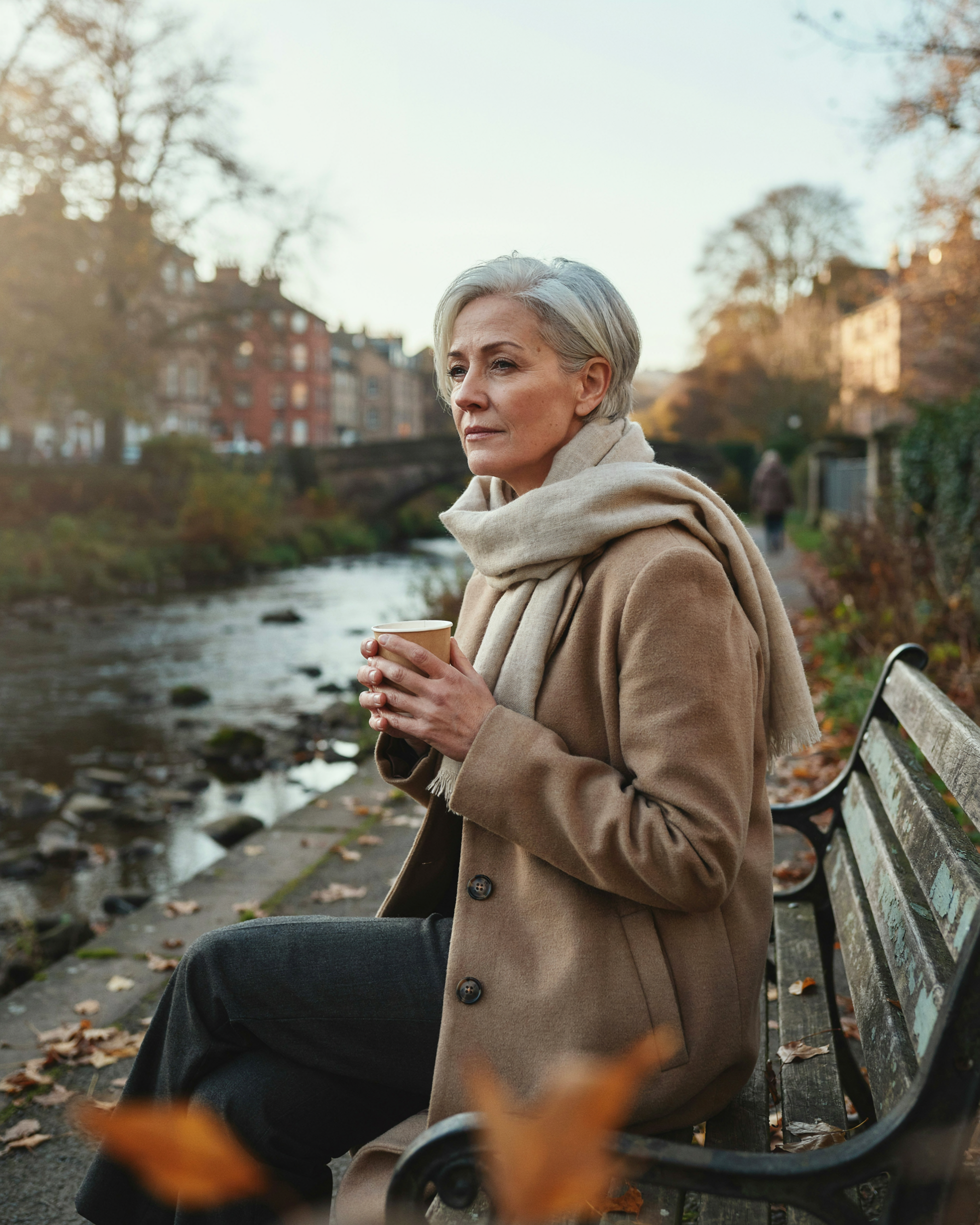 Woman wrapped in a scarf with a warm drink beside the Water of Leith in Stockbridge, Edinburgh