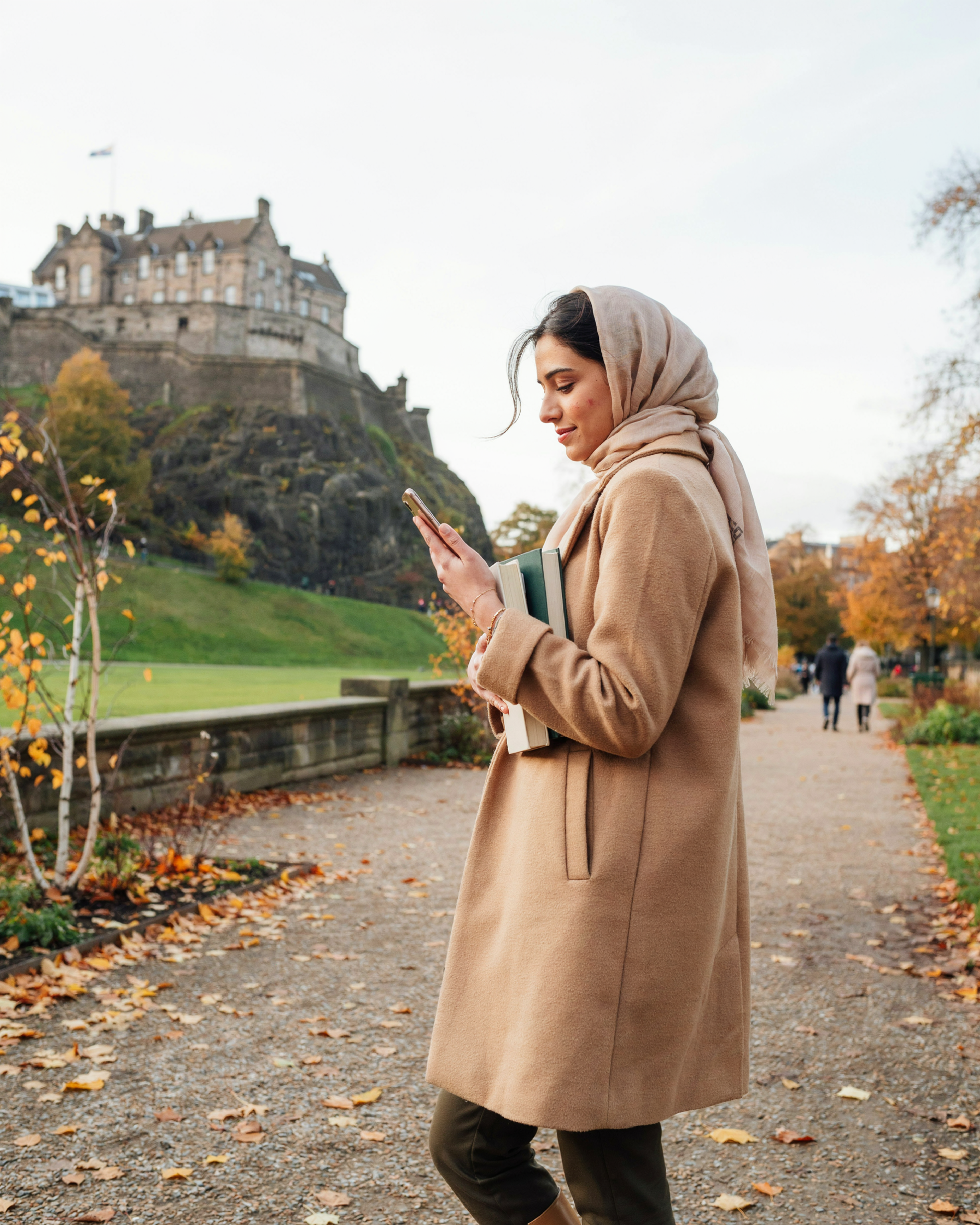 International student walking through Princes Street Gardens in Edinburgh with the castle behind