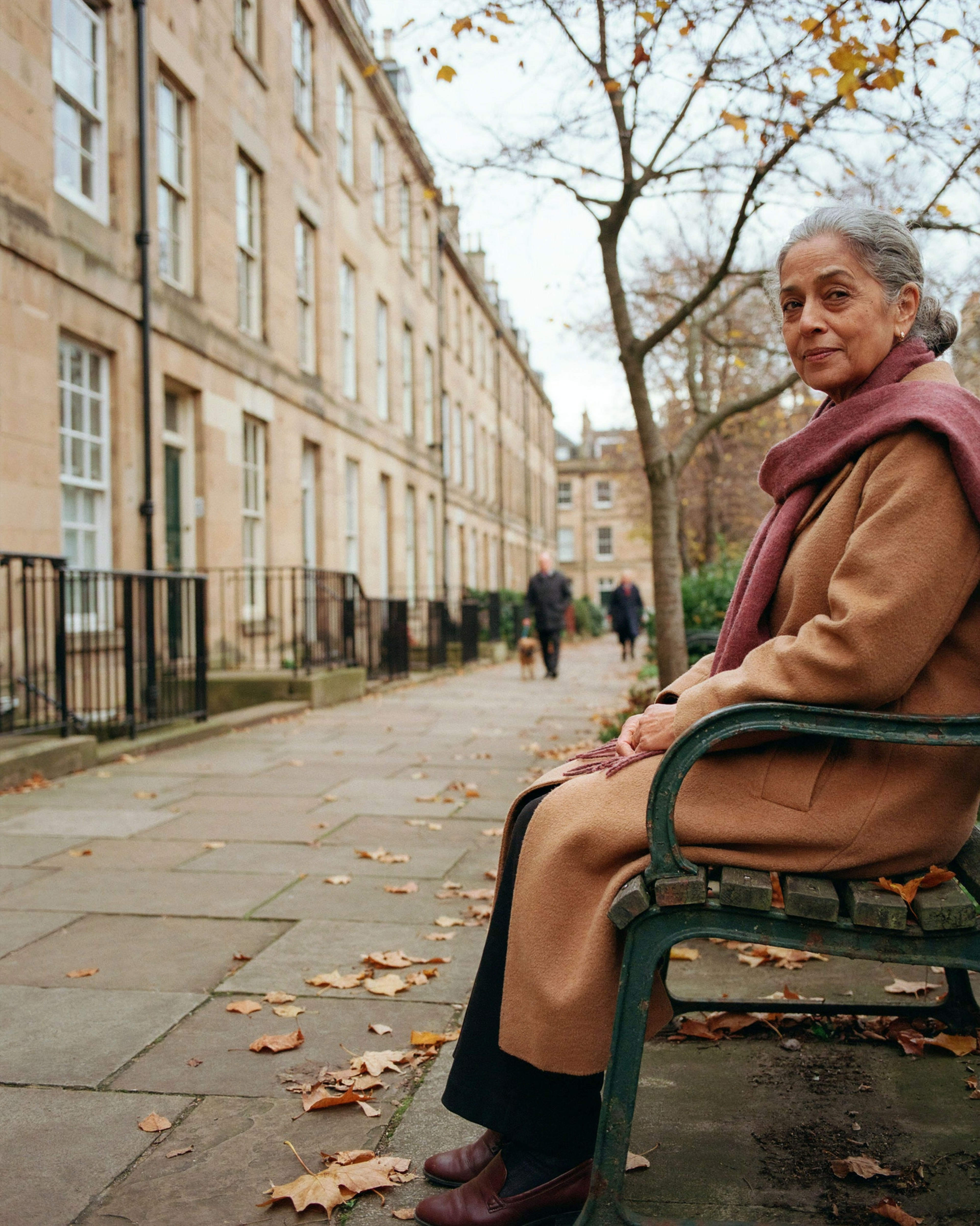 Older woman resting on a bench in a garden square in Edinburgh's Southside in autumn