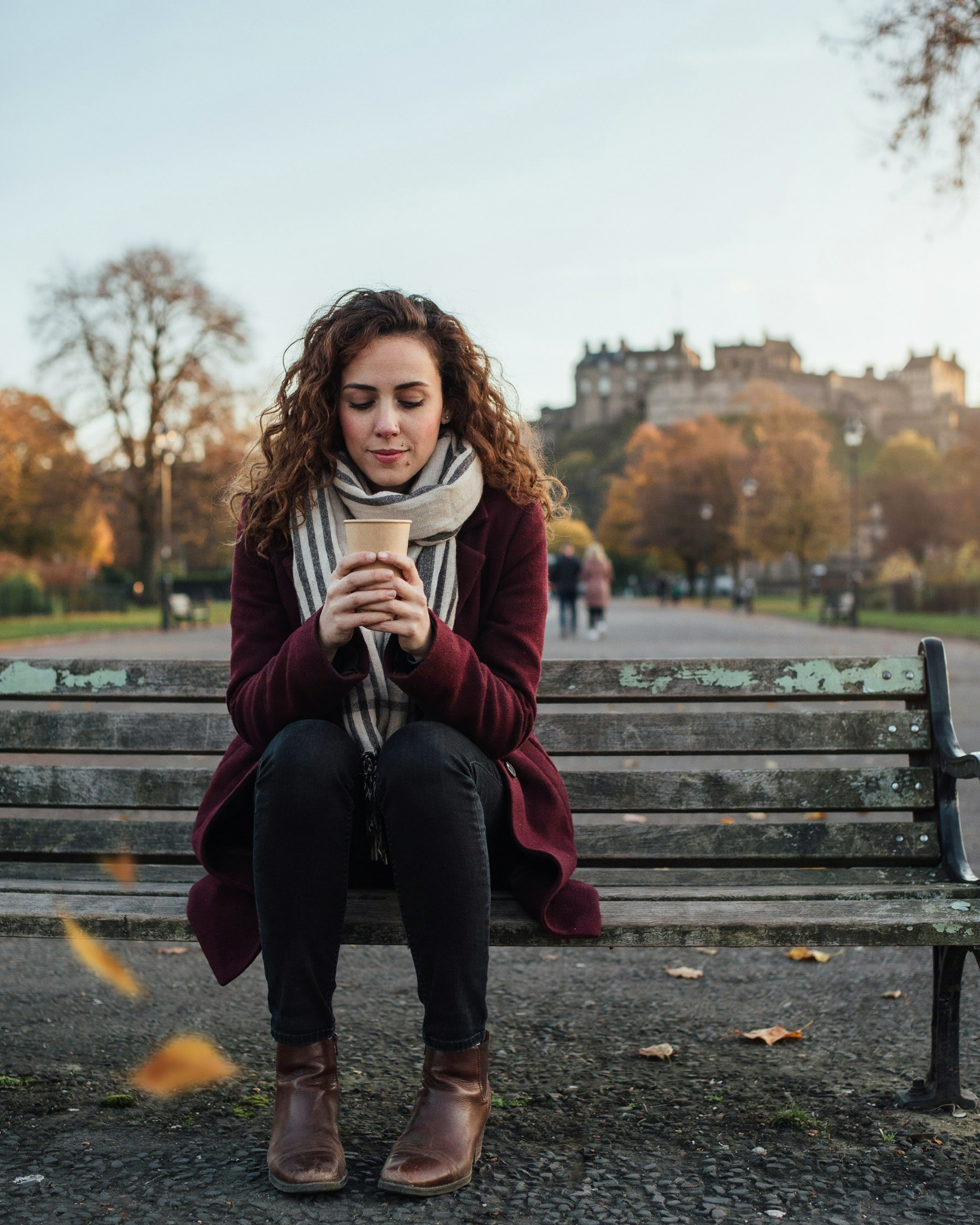Student wrapped in a scarf with a warm drink in Princes Street Gardens, Edinburgh