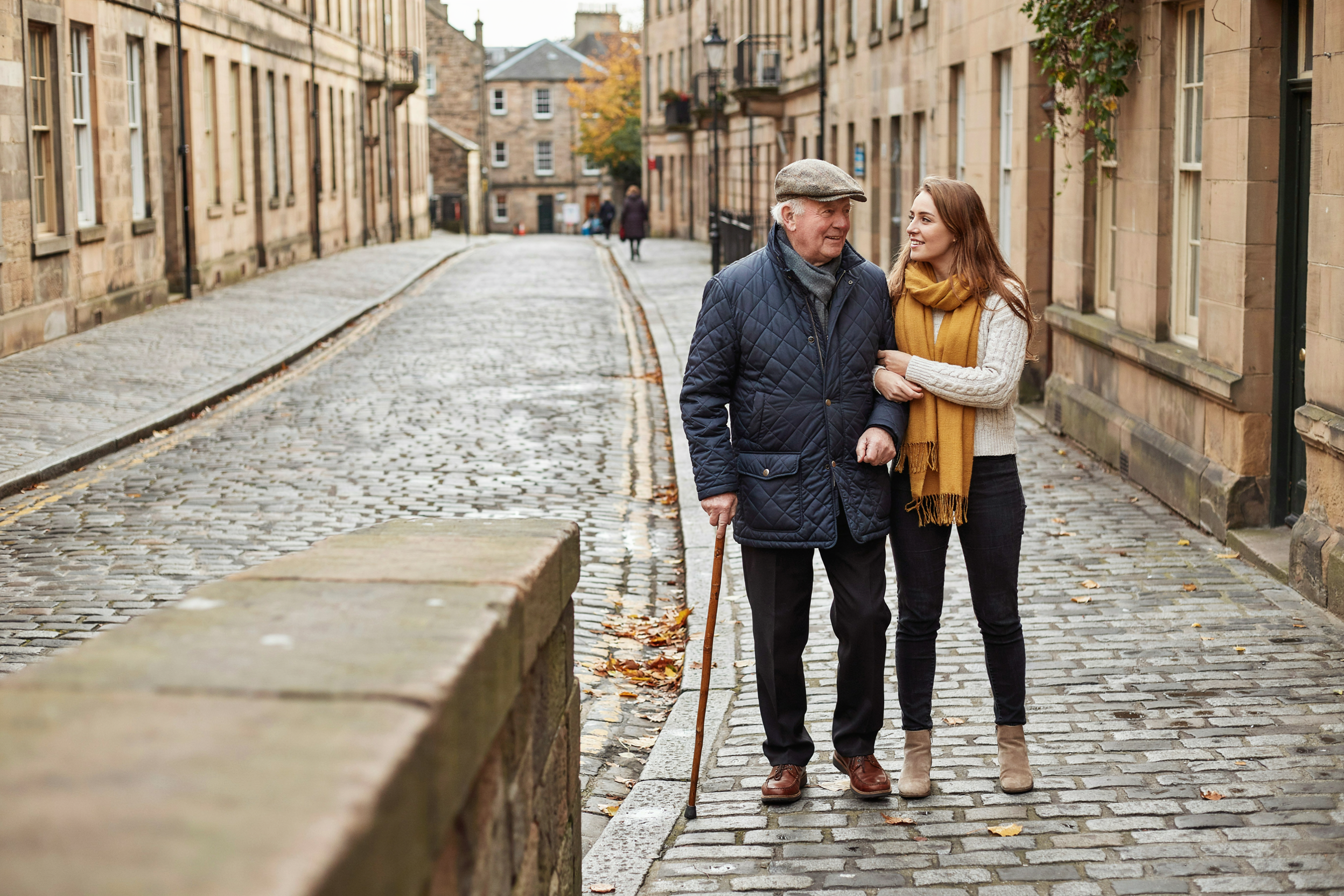 Older man walking arm in arm with his granddaughter on a cobbled Old Town street in Edinburgh