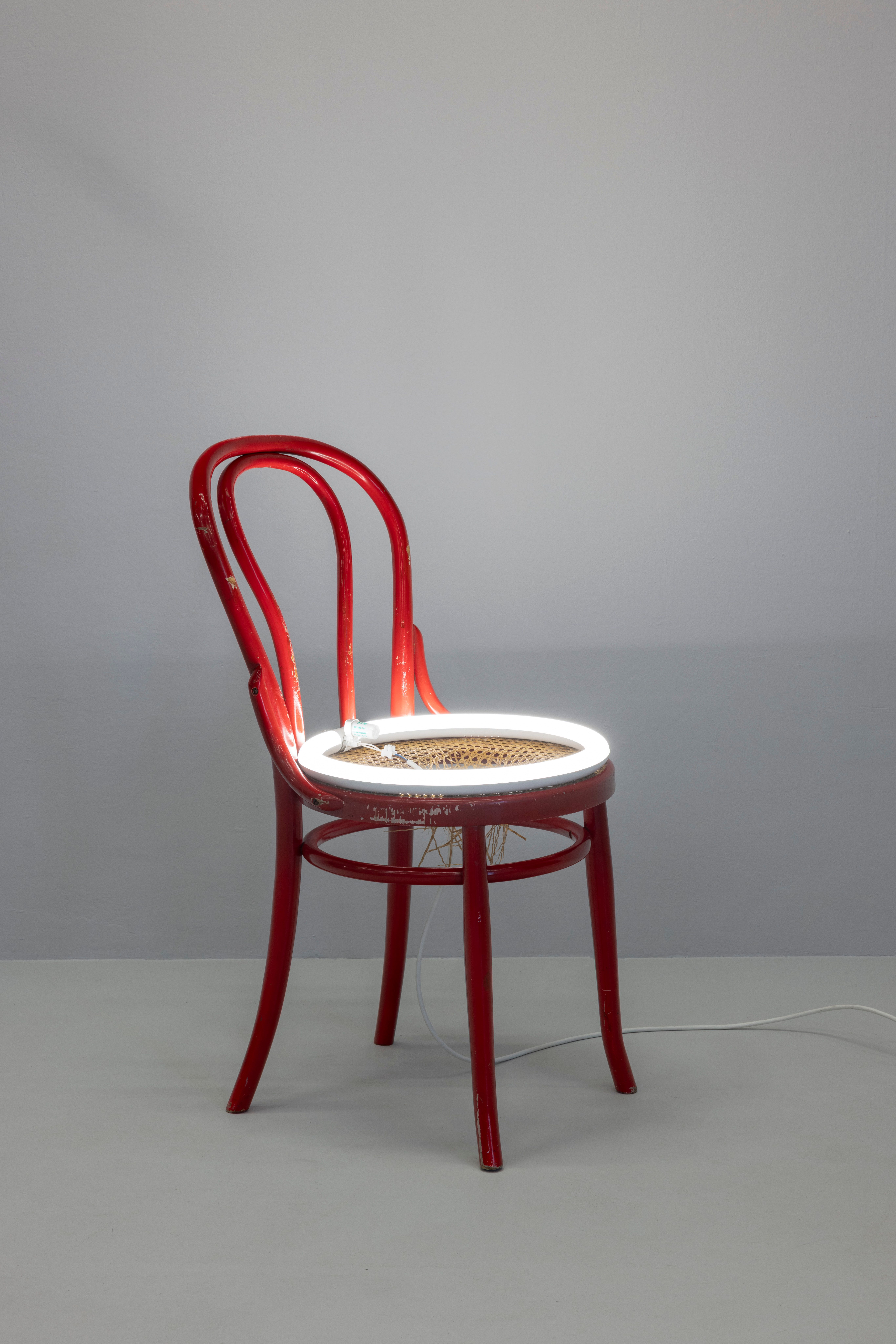 Davide Stucchi's sculpture A red Thonet-style wooden chair with a circular white neon light glowing on its woven seat.