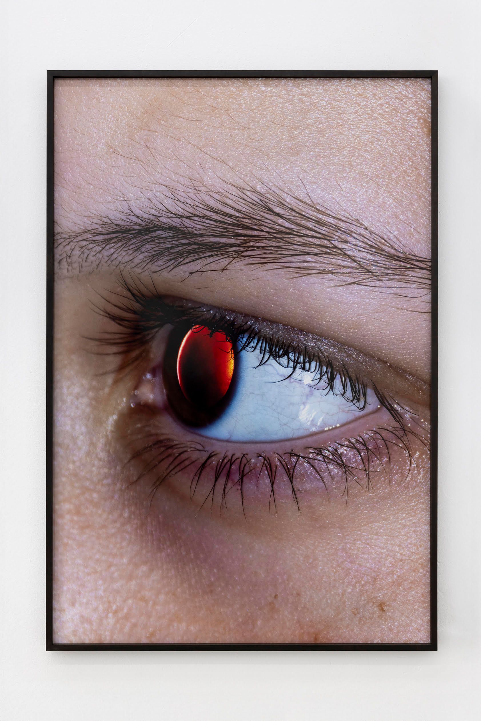 A close-up photograph of a person's eye featuring a glowing, deep red iris that resembles a solar eclipse or a celestial orb.