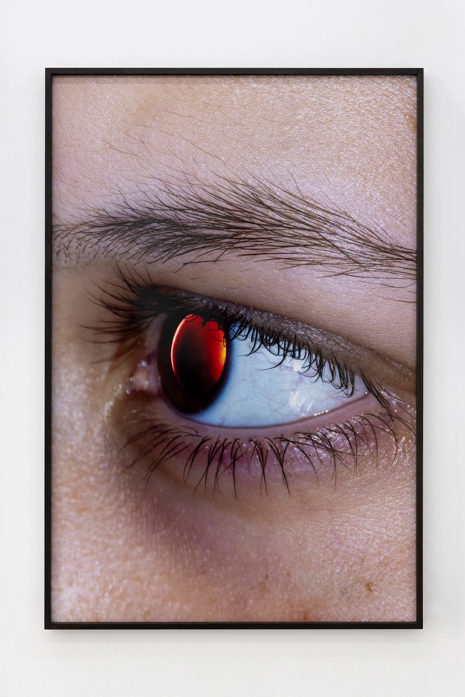 A close-up photograph of a person's eye featuring a glowing, deep red iris that resembles a solar eclipse or a celestial orb.