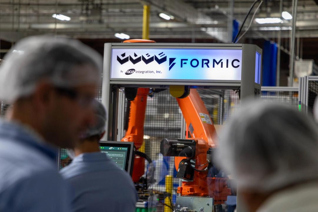 Plant visitors in hairnets watch a Formic and Focus Integration CUBE robotic palletizer running on a production floor