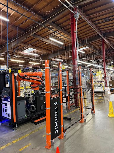 Formic robotic palletizer cell with orange safety fencing at the end of a production line on a manufacturing floor.