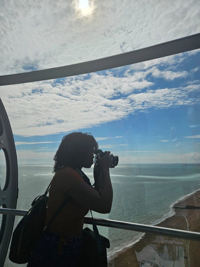Mona silhouetted against the sea, camera raised to her eye