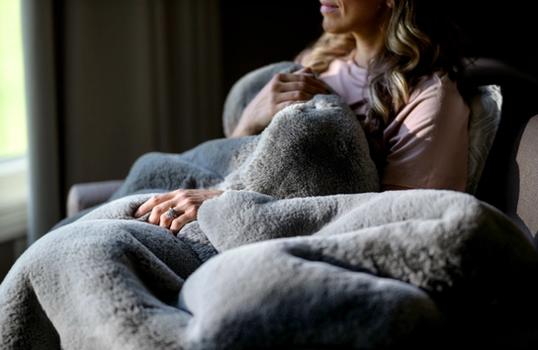 Woman snuggling in chair with Faux Fur Blanket in color Fog