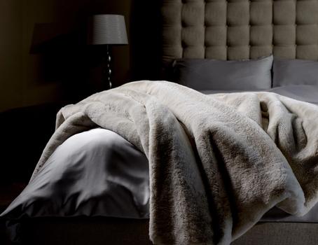 Faux Fur Blanket draped on end of bed in color Almond