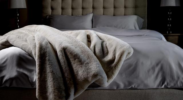 Faux Fur Blanket draped on end of bed in color Almond