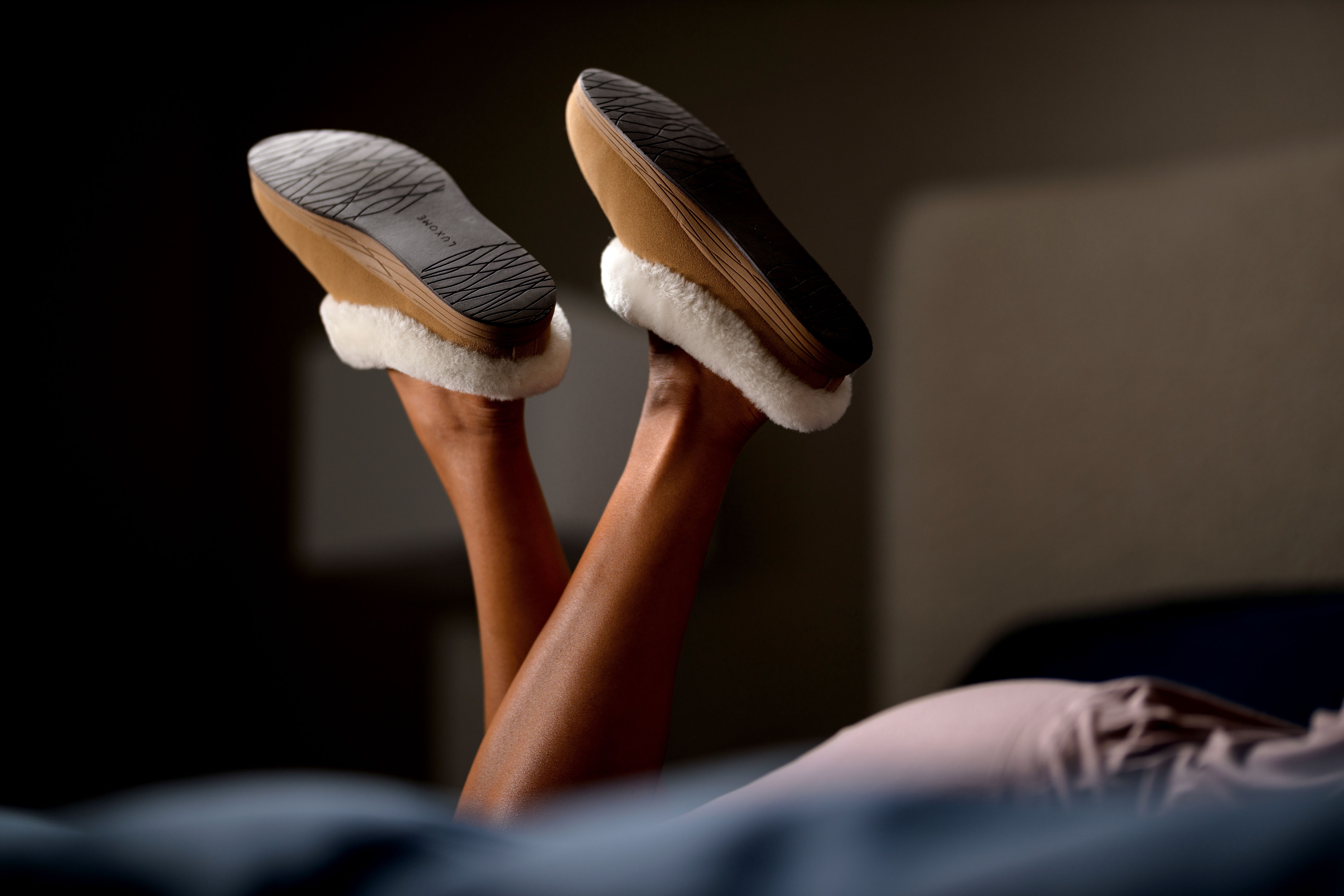 Woman's kicking feet on bed wearing Chestnut Signature Slippers