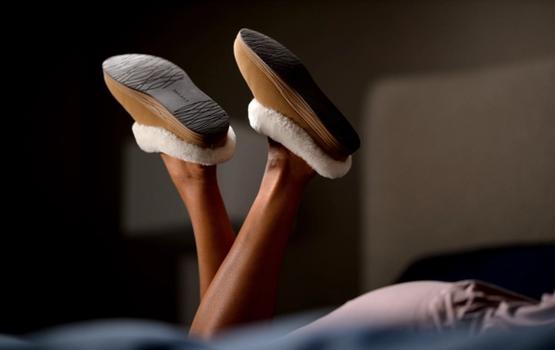 Woman's kicking feet on bed wearing Chestnut Signature Slippers