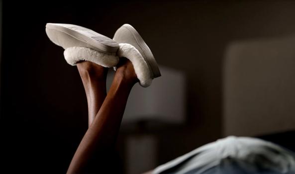 Woman's kicking feet on bed wearing Birch Signature Slippers