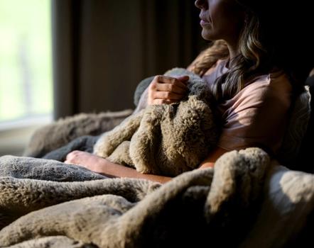 Woman snuggling in chair with Faux Fur Blanket in color Truffle