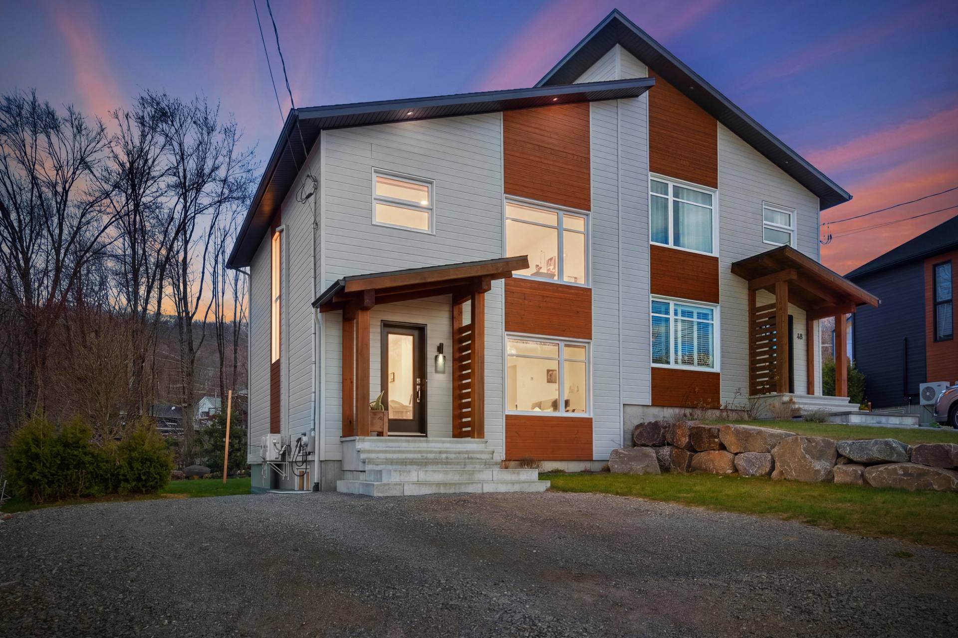 Duplex moderne au revêtement blanc et bois, entrée éclairée sous un ciel de crépuscule