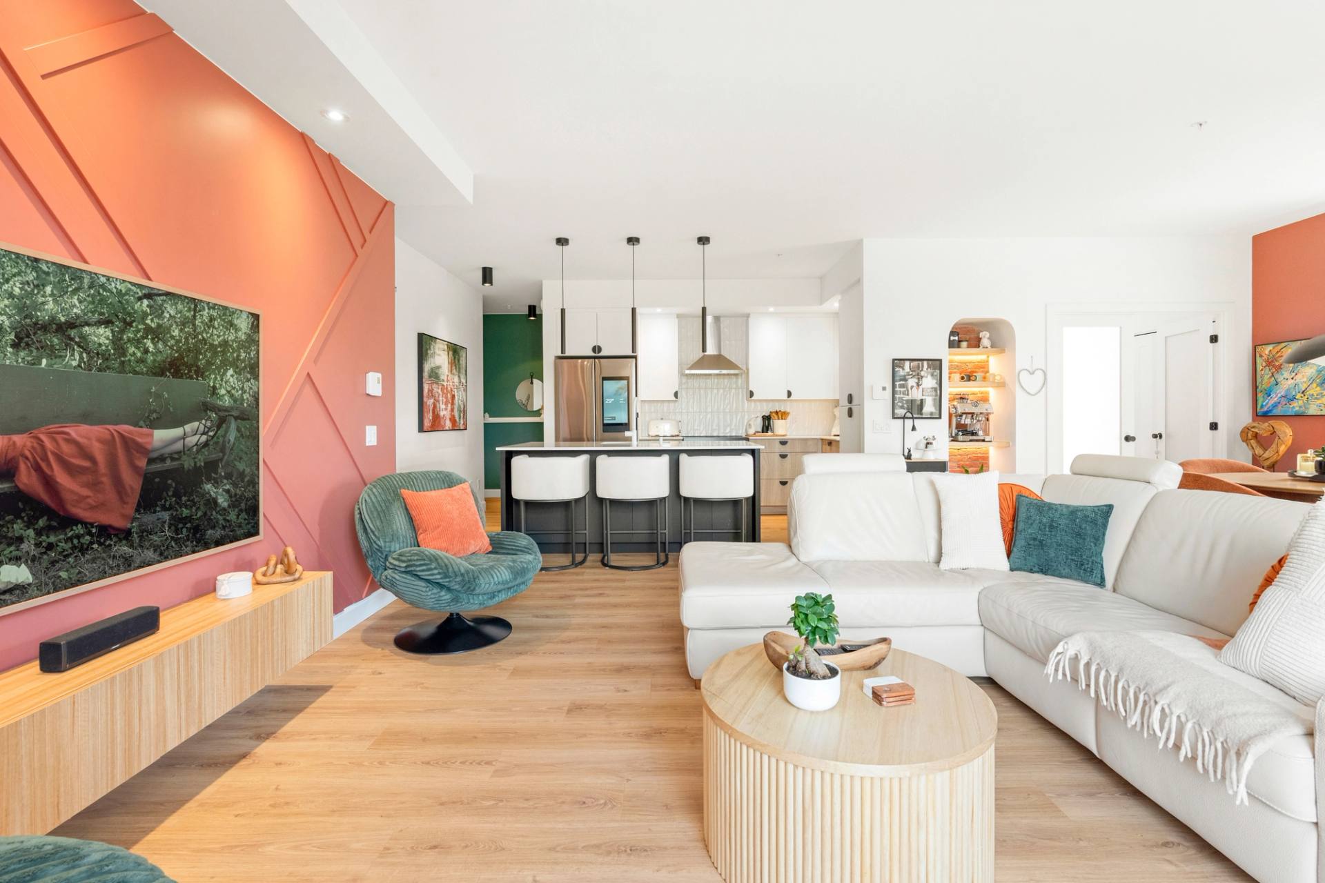 Aire ouverte d'un condo, mur corail, sofa blanc et cuisine ouverte au fond
