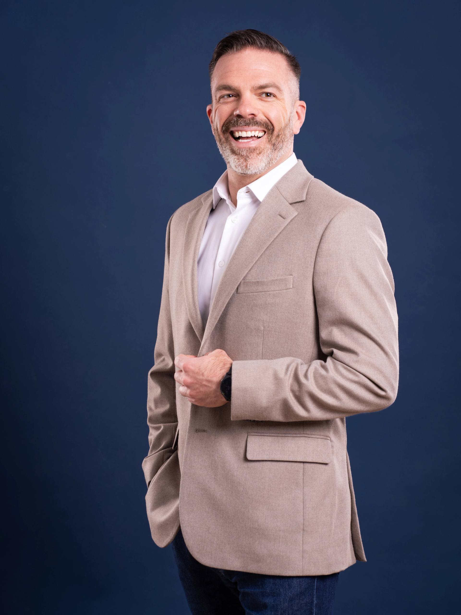 Portrait corporatif d'un homme en veston beige souriant, sur fond bleu nuit