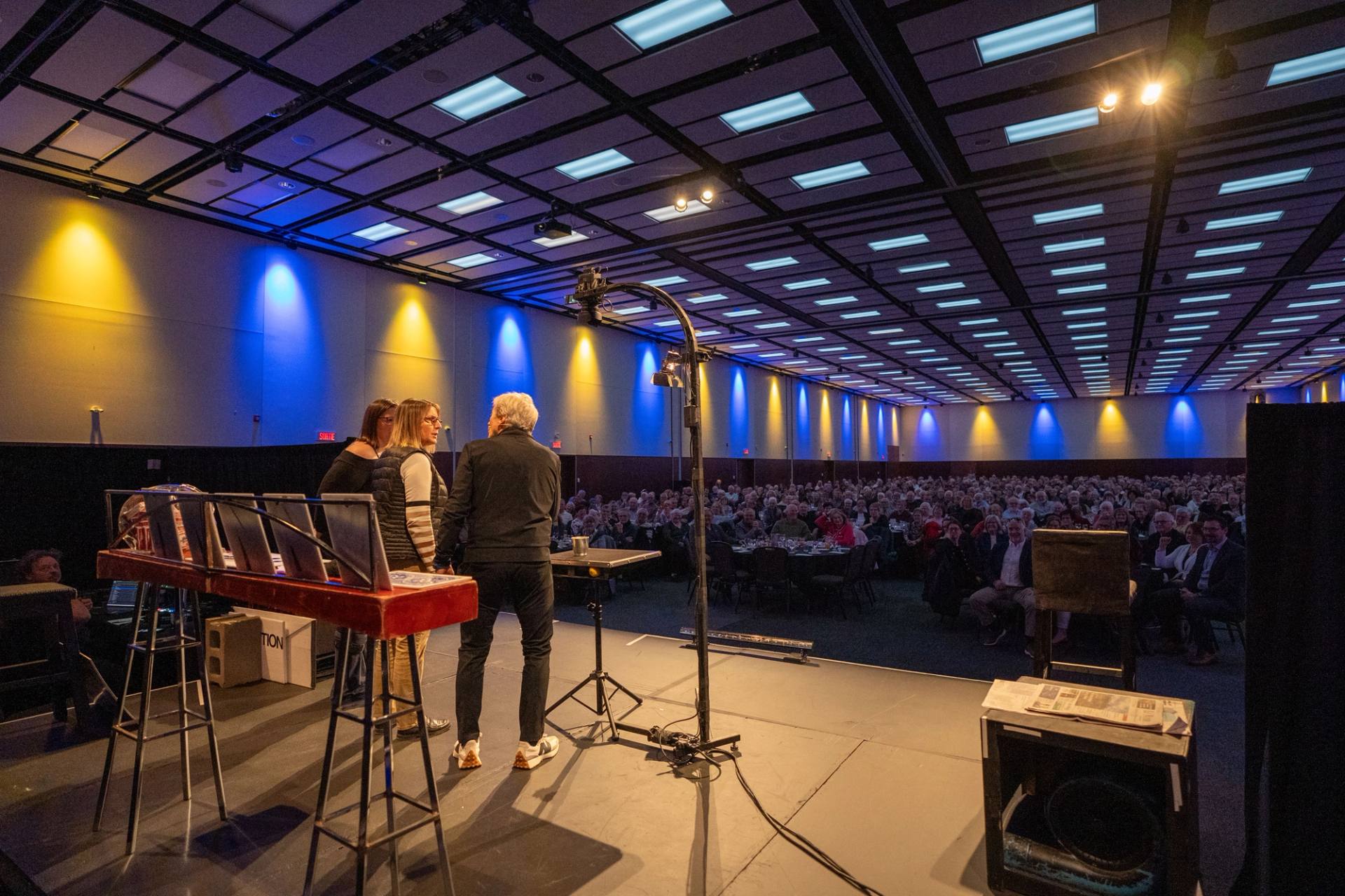 Salle de spectacle vue de l'arriere, scene eclairee en bleu et rangees de spectateurs