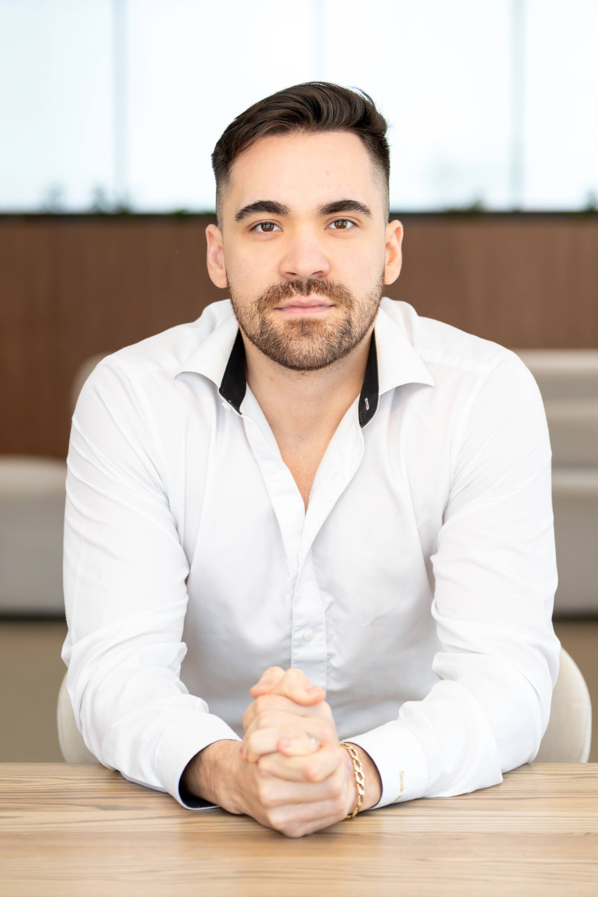 Homme en chemise blanche, mains jointes, assis dans un bureau lumineux