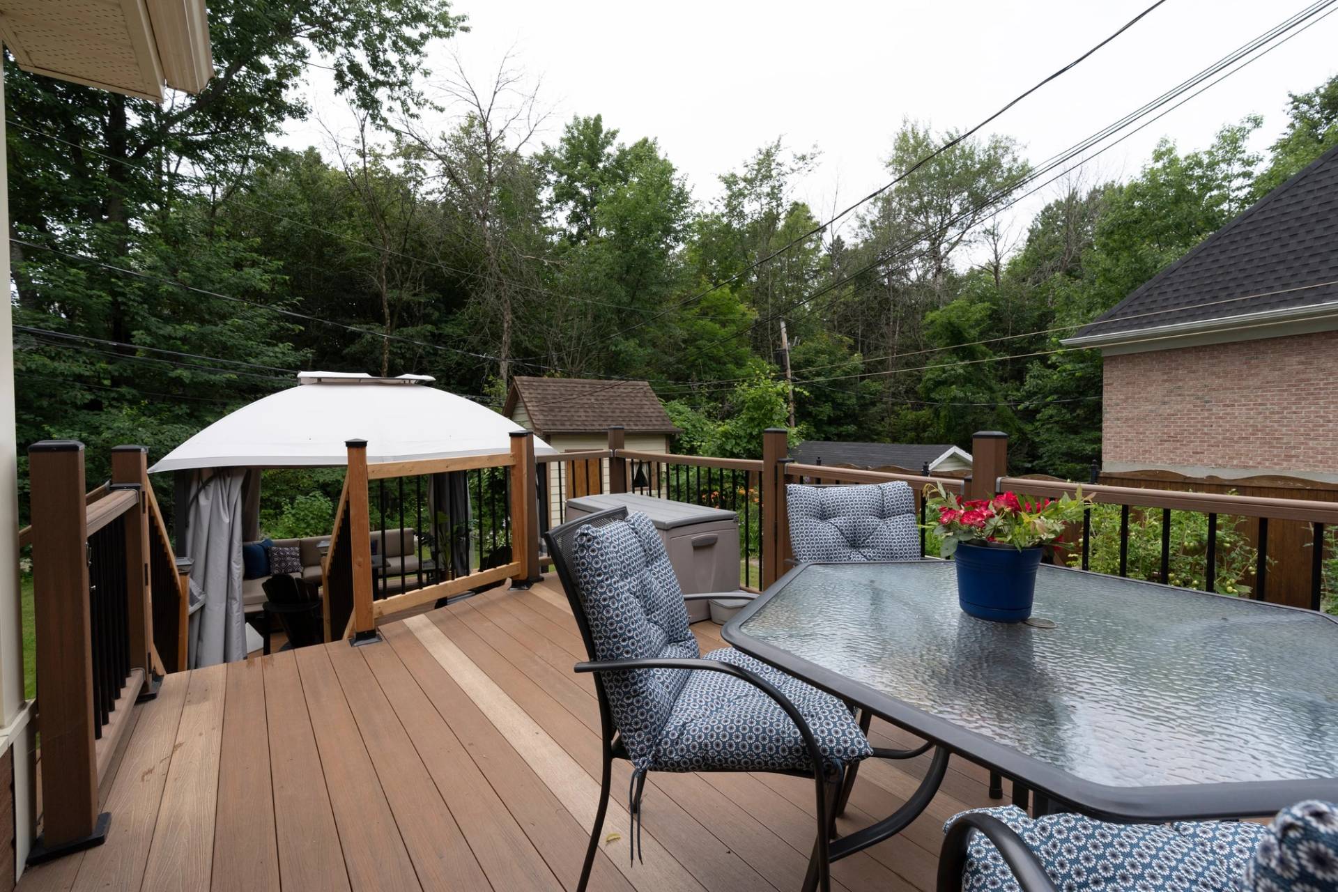 Terrasse de bois avec table de verre, chaises et gazebo, sous un ciel entièrement blanc