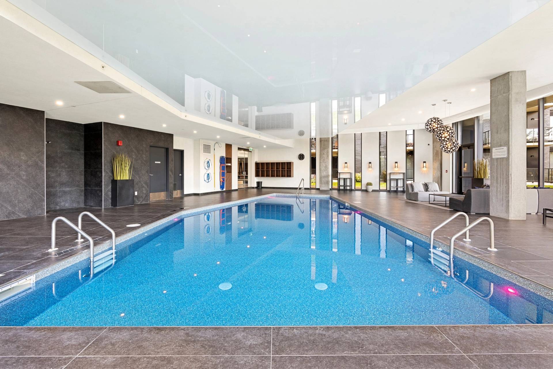 La même piscine intérieure, eau turquoise et plafond clair, fauteuils au fond de la salle